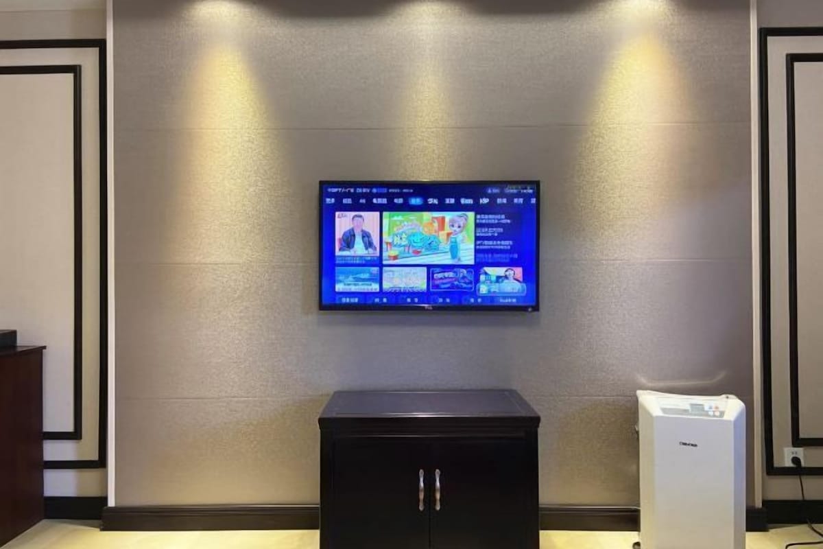 Un televisor de pantalla plana fijado a una pared texturizada, un mueble negro debajo y un dispositivo blanco a la derecha.