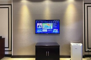 Un televisor de pantalla plana fijado a una pared texturizada, un mueble negro debajo y un dispositivo blanco a la derecha.