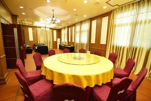 Un salón de conferencias con una mesa redonda, sillas rojas y una lámpara de araña.