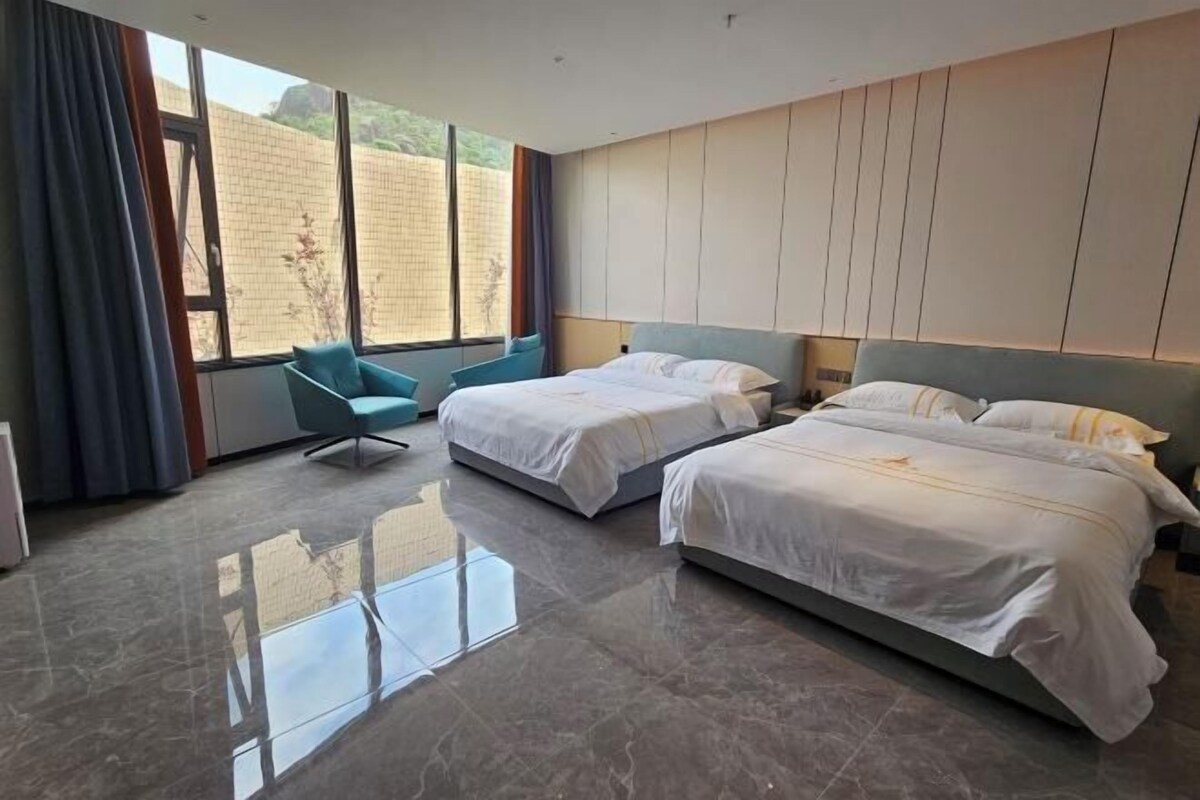 Una habitación de hotel moderna con dos camas, un ventanal grande y una silla azul.