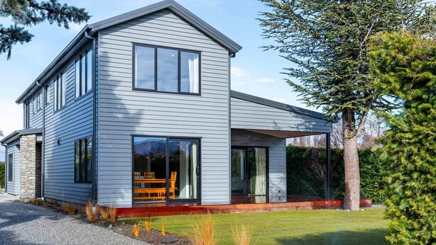 A modern two-story house with a large glass door entrance, a stone foundation, and a well-maintained lawn.