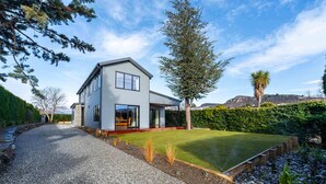 A modern two-story house with a gravel driveway, a well-maintained lawn, and a variety of trees and shrubs.