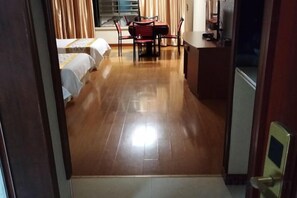 Quarto de hotel com piso de madeira, uma cama, uma escrivaninha e uma cadeira.
