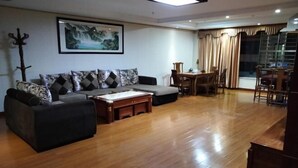Una sala de estar con sofá, reposapiés y mesa de centro. Hay una mesa de comedor con sillas y un cuadro en la pared.