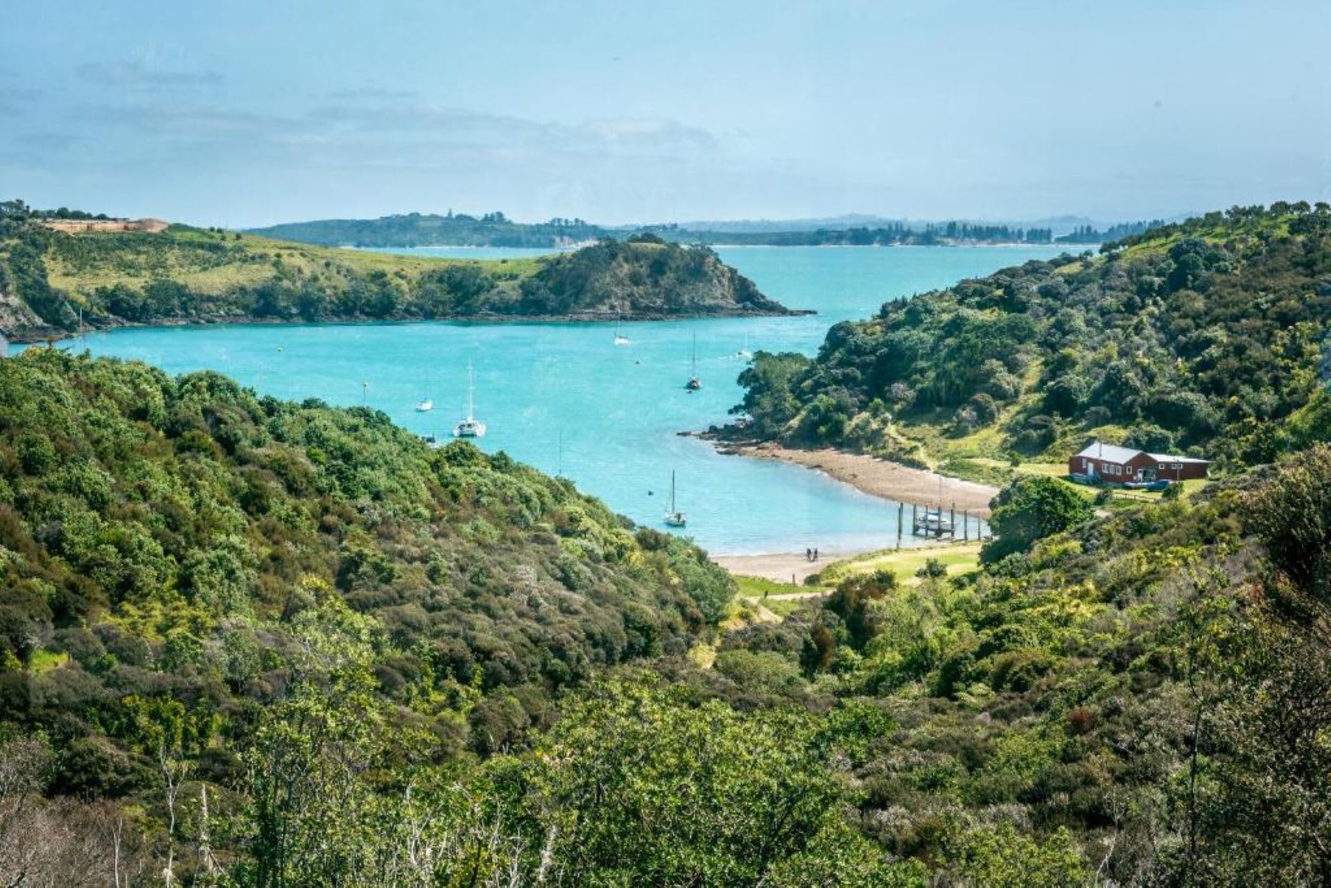 Un paysage côtier avec une plage, des bateaux et une maison.