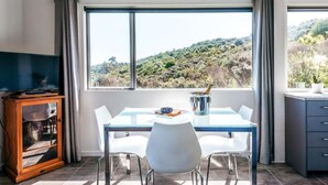 Un comedor con una mesa, sillas, un televisor y vistas a un paisaje montañoso.