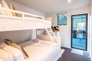 A bunk bed room with a ladder, a small desk with a teddy bear, and a door leading to an outdoor area.