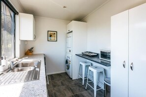 A compact kitchen with a sink, washing machine, and a microwave. There are two stools and a small countertop.