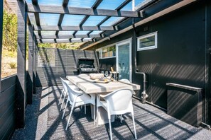 A covered patio with a grill, white chairs, and a table set for dining.