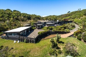 A modern building with a flat roof, surrounded by lush greenery and hills.
