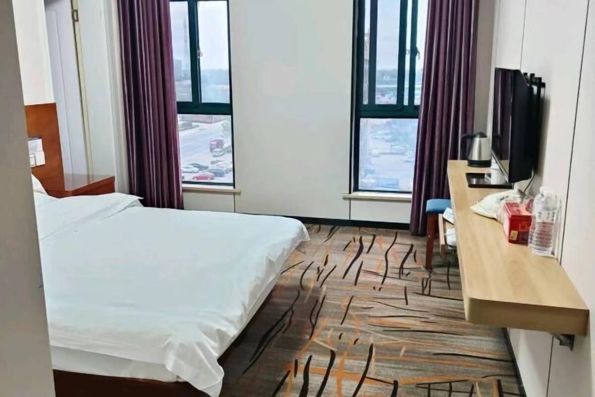 Ein Hotelzimmer mit Bett, Schreibtisch mit Computer, Fernseher und Fenster mit Stadtblick.