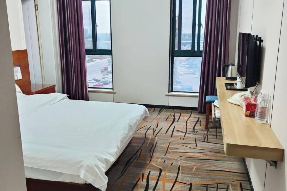 Ein Hotelzimmer mit Bett, Schreibtisch, Computer, Stuhl und einem Fenster mit Vorhängen.