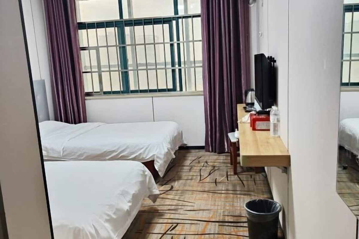 Ein Hotelzimmer mit zwei Betten, einem Schreibtisch mit Stuhl, einem Fernseher und einem Fenster mit Gitterstäben.