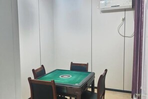 A room with a green pool table, four chairs, a white wall, and a door with a purple curtain.