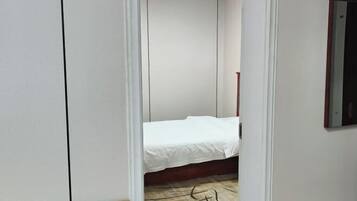 Un couloir étroit mène à une chambre à coucher qui contient un lit et un plancher en bois.