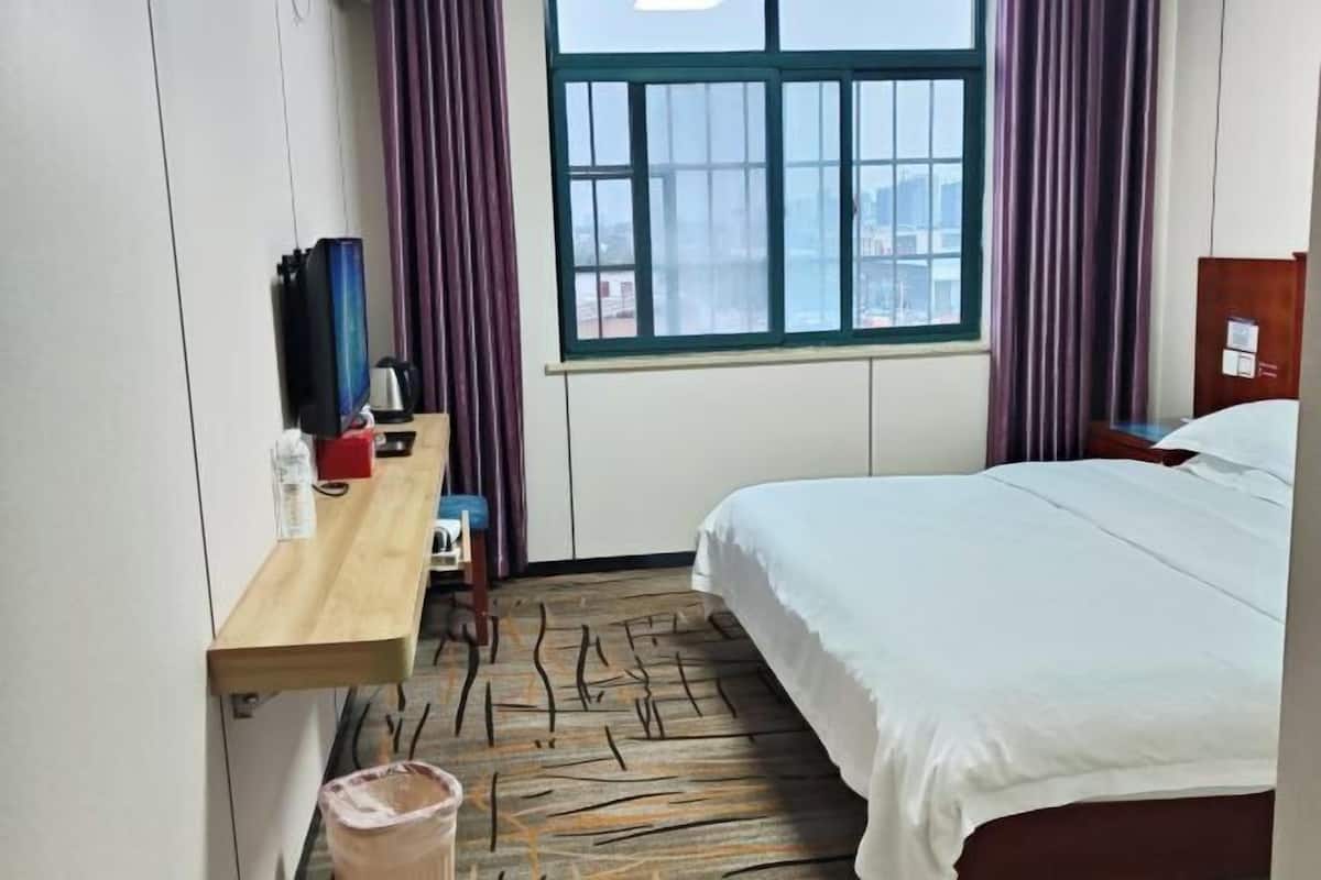 Ein Hotelzimmer mit Bett, Schreibtisch mit Computer, Fenster mit Vorhängen und Blick auf die Stadt.