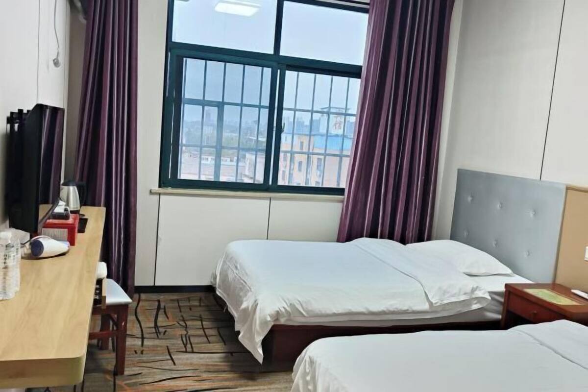 Ein Hotelzimmer mit zwei Betten, einem Schreibtisch mit Stuhl, einem Fernseher und einem Fenster mit Vorhängen.