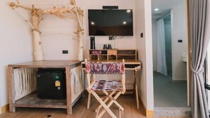 A compact room with a wooden desk, a foldable chair, a flat-screen TV, and a small refrigerator. - B Innspire Hotel (Chiang Mai)