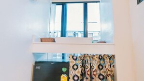 A room with a window, a small table with a basket, a refrigerator, and patterned curtains. - B Innspire Hotel (Chiang Mai)