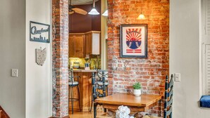 A dining area with a brick wall, a framed poster, and a wooden table with chairs. - Downtown Cleveland Loft | Walk to Stadiums & Convention Center (Cleveland)