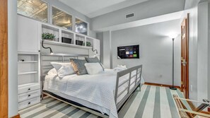 A bedroom with a bed, built-in shelving, a TV, and a wooden door.