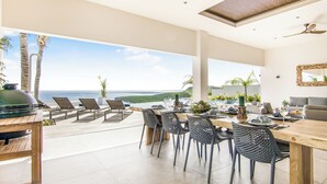 Un amplio comedor con vistas al océano, muebles modernos y un ventilador de techo.