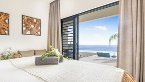 Un dormitorio con una cama grande, vista al océano y un balcón con mesa y sillas.