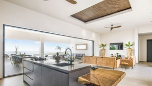Una cocina moderna con una isla grande, un comedor con vistas y una sala de estar con sofá y televisión.
