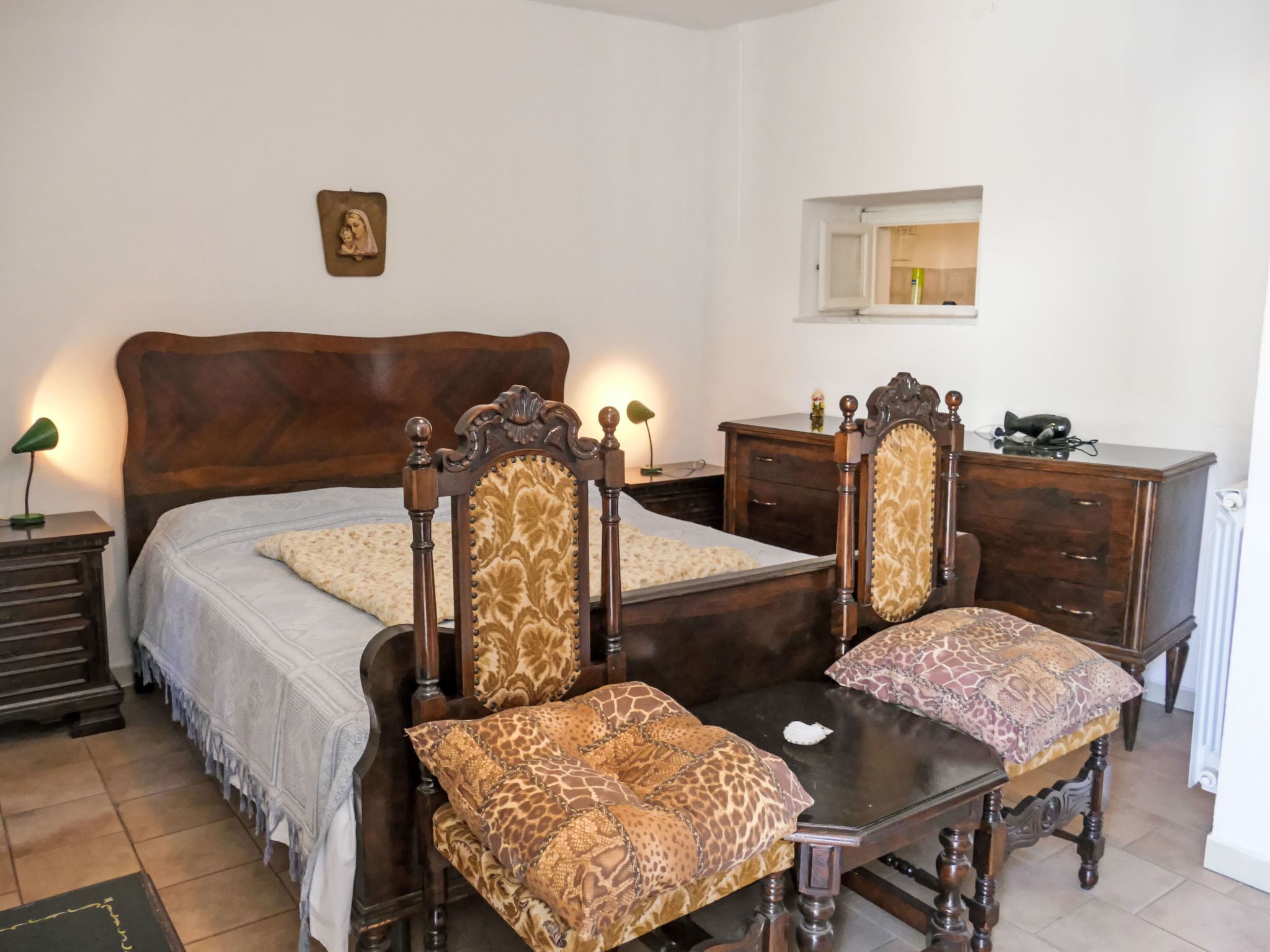 A bedroom with a large bed, two nightstands, a dresser, a mirror, and a small statue on the wall.