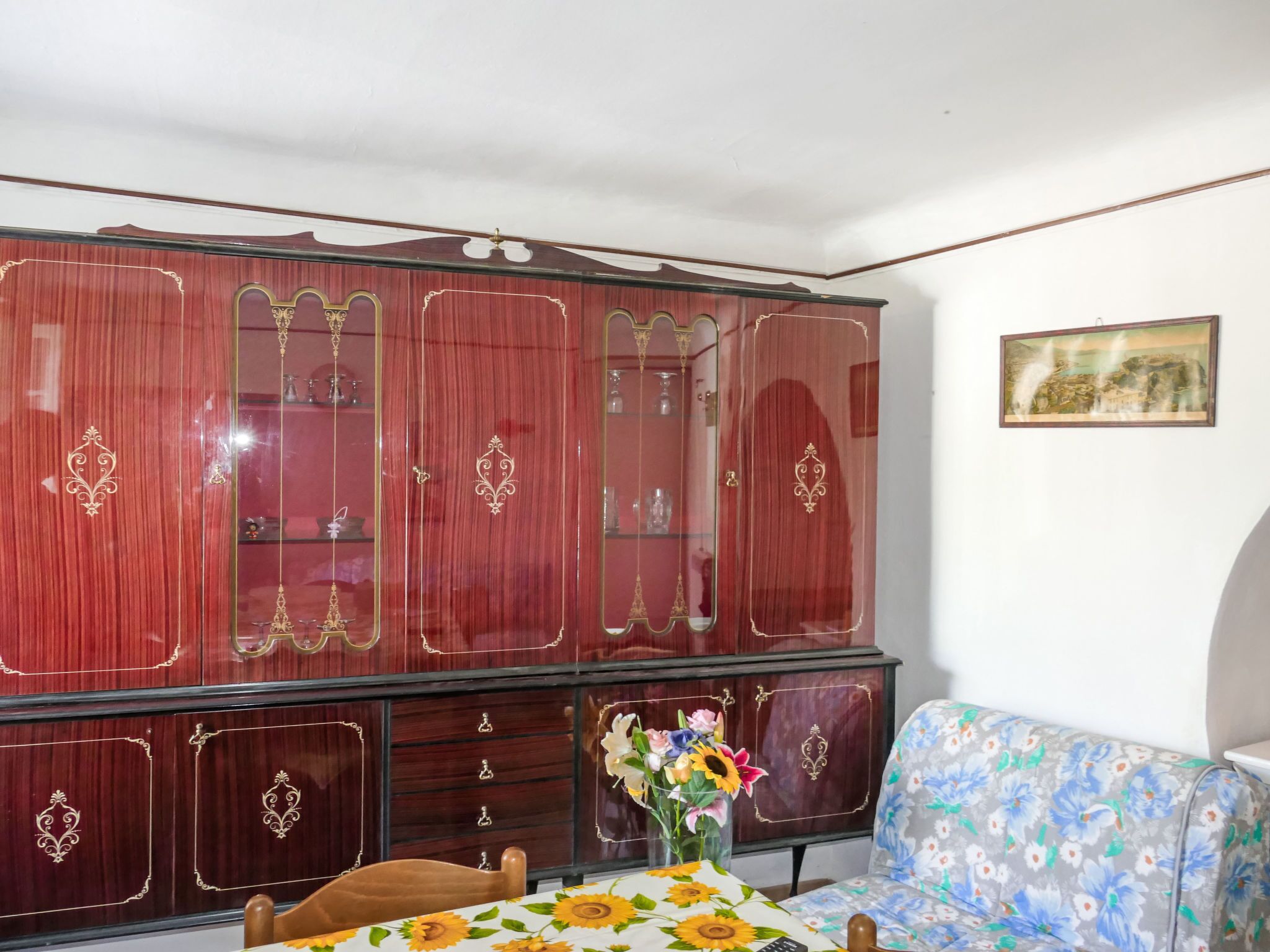 Una habitación con un armario grande de madera, un sofá floral y una mesa con un jarrón de flores.