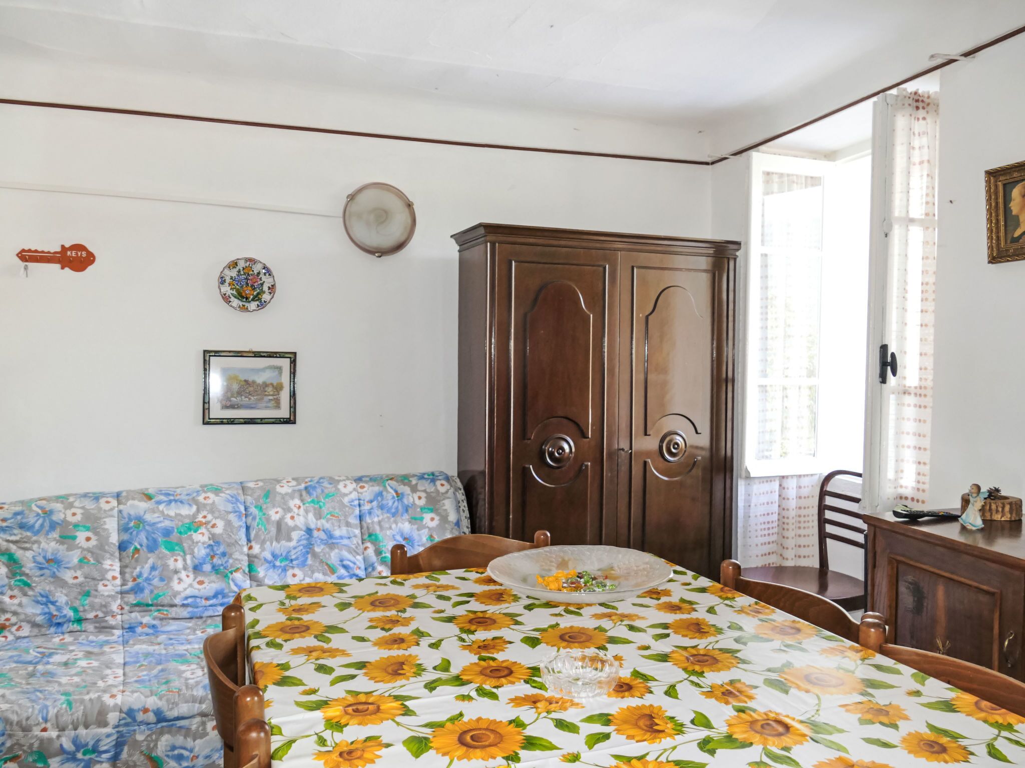 A room with a bed, a wooden wardrobe, a floral sofa, and a dining table with chairs.