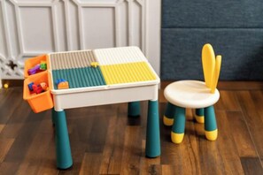 Una mesa de juegos para niños con una silla, suelo de madera y una pared blanca con un panel decorativo.