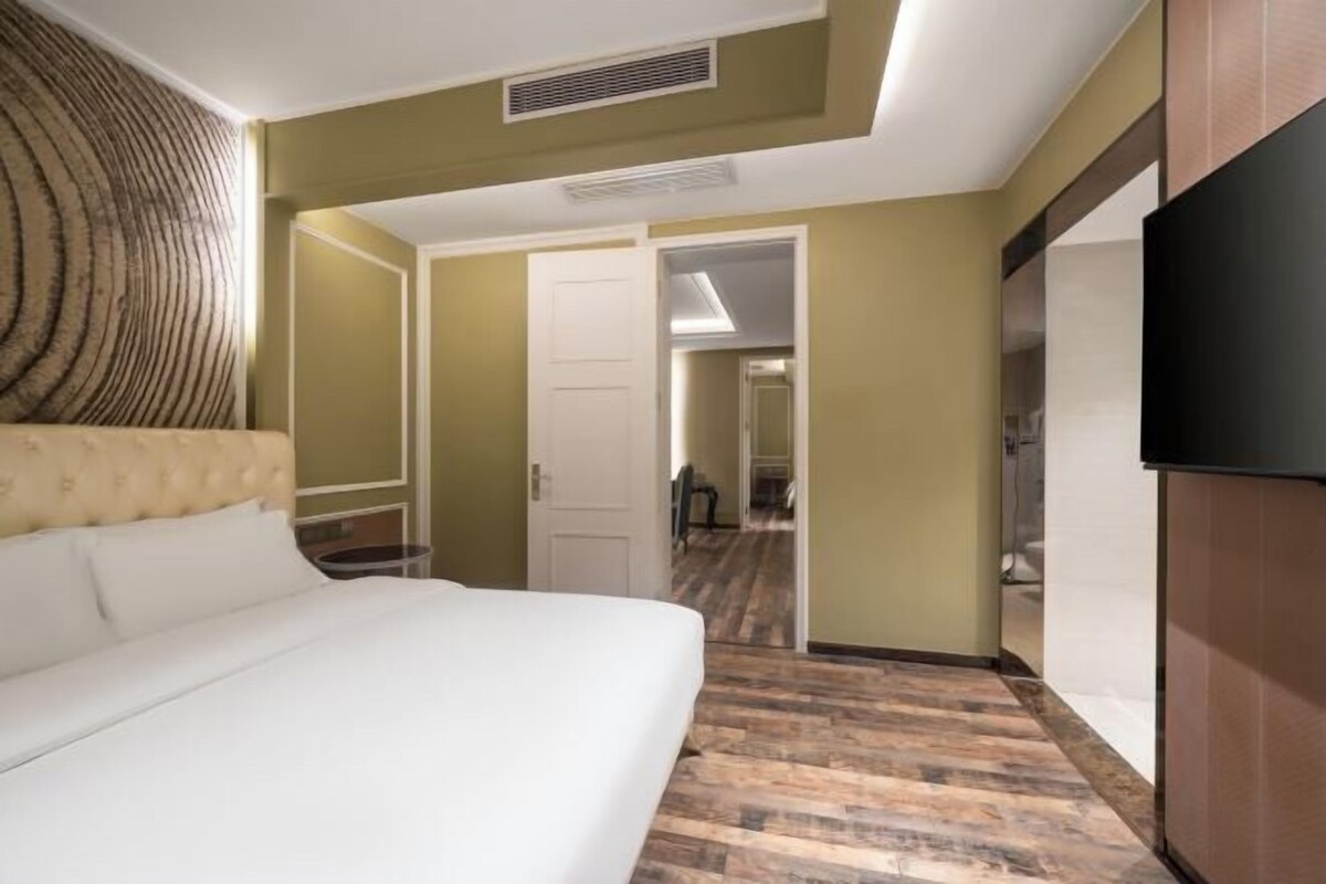 Ein Hotelzimmer mit einem großen Bett, einem Schrank, einem Fernseher und einer Tür zu einem weiteren Raum.