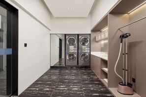 Een gang met een wasmachine, een stofzuiger en een spiegel.