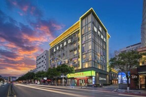 A multi-story hotel with a modern design, located on a city street with a clear sky. - McQueen Hotel (Dongguan)