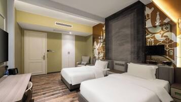 A hotel room with two beds, a desk, a chair, a TV, and a decorative wall.