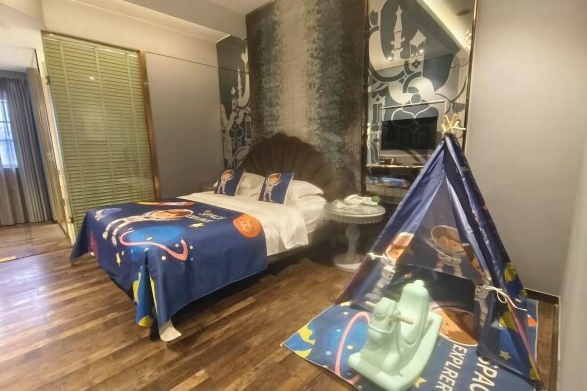Ein Hotelzimmer mit einem Bett, das mit einer farbenfrohen Tagesdecke bezogen ist, einem kleinen runden Tisch mit einer Lampe und einer zeltartigen Struktur mit Designs zum Thema Weltraum.