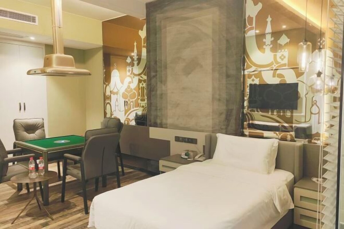 Ein Hotelzimmer mit einem Bett, einem Schreibtisch mit grüner Tischplatte, einem Sessel, einer Couch und einem an der Wand montierten Fernseher.