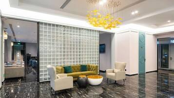 A modern lobby with a marble floor, a yellow sofa, white armchairs, and a large glass partition.