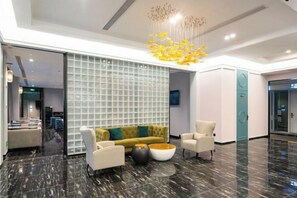 A modern lobby with a marble floor, a yellow sofa, white armchairs, and a large glass partition. - McQueen Hotel (Dongguan)