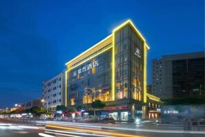 A multi-story hotel with illuminated signage, a prominent entrance, and a street view with moving traffic. - McQueen Hotel (Dongguan)