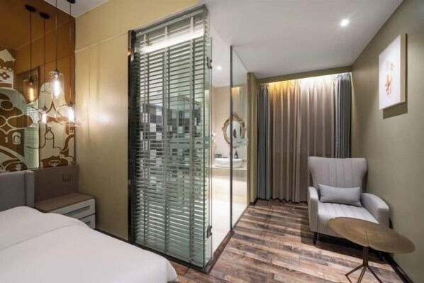 Ein Hotelzimmer mit einem Bett, einer Sitzecke mit einem Sessel, einer Glaskabine und Blick ins Bad.