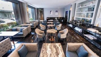 Een moderne hotellobby met zitgedeeltes, een marmeren bijzettafeltje en uitzicht op de parkeerplaats.