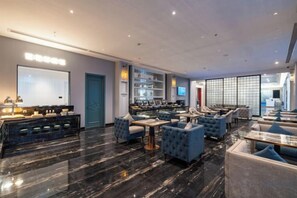 A modern hotel lobby with a bar area, seating arrangements, and a large screen. - McQueen Hotel (Dongguan)