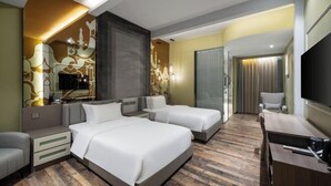 Ein Hotelzimmer mit zwei Betten, einem Schreibtisch, einem Fernseher und einem Spiegel.