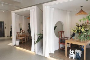 Une pièce comprenant une table à manger en bois, des chaises, un rideau blanc et un luminaire suspendu.