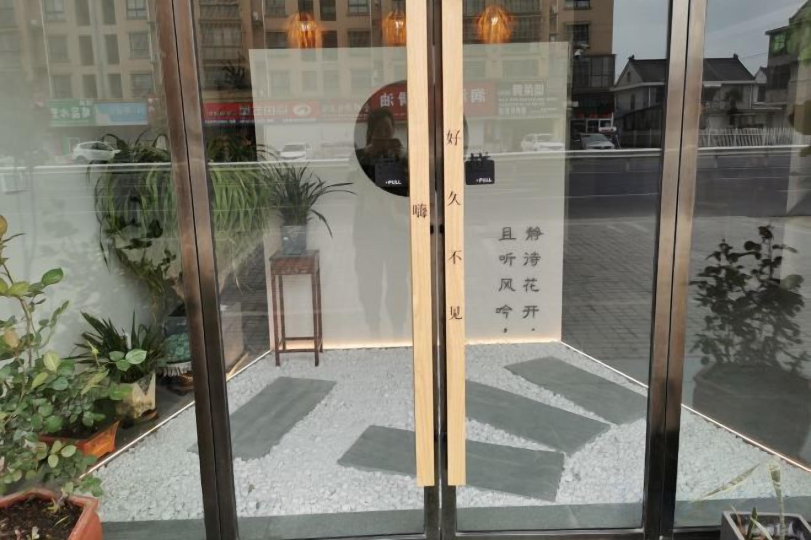 Ein Hotel Eingang mit Glastür, einem kleinen Tisch, einem Stuhl und Topfpflanzen.