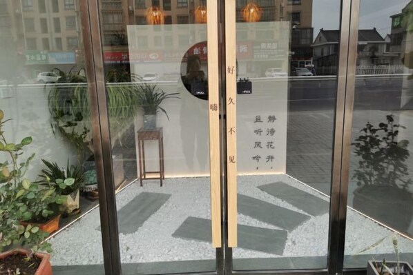 Ein Hotel Eingang mit Glastür, einem kleinen Tisch, einem Stuhl und Topfpflanzen.