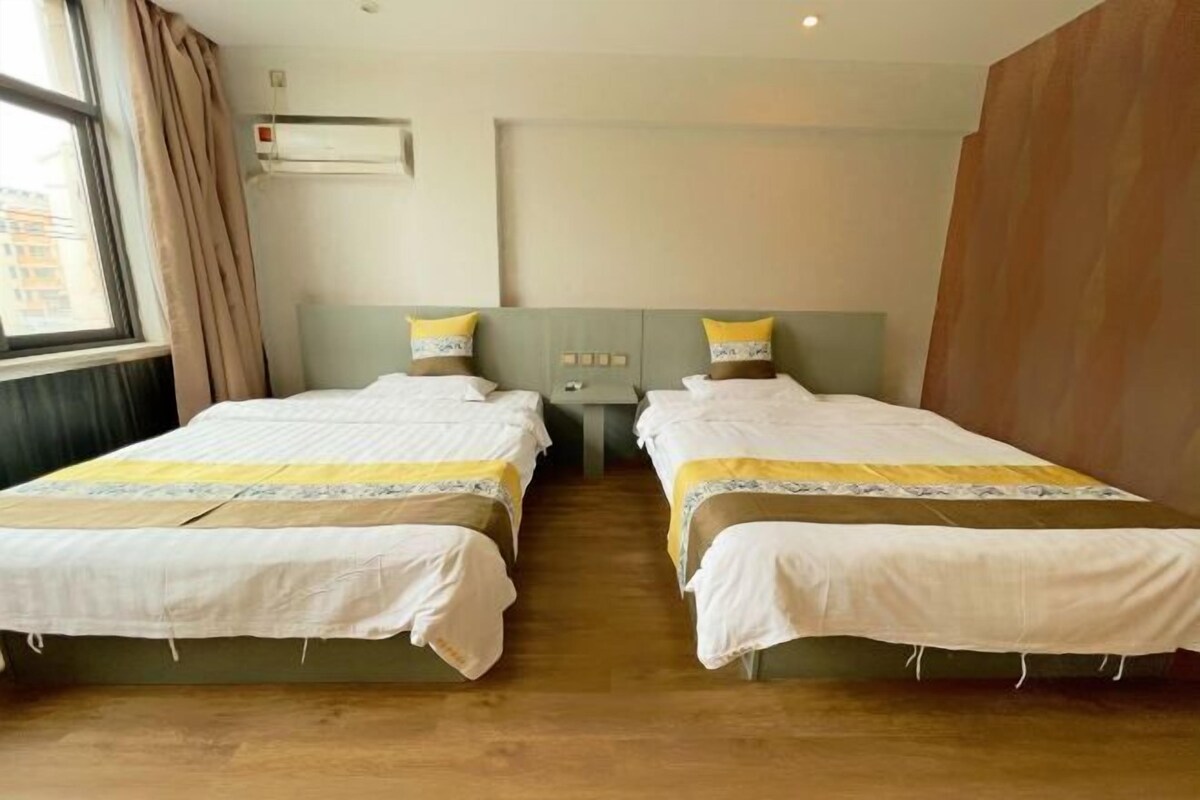A hotel room with two beds, a window with curtains, an air conditioning unit, and a wooden wall.