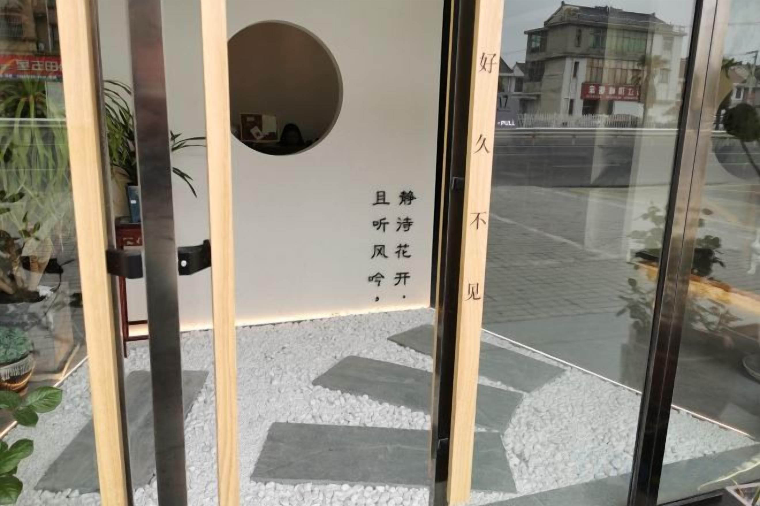 A glass door with a circular cut-out, a white wall with Chinese characters, and a reflection of a building outside.